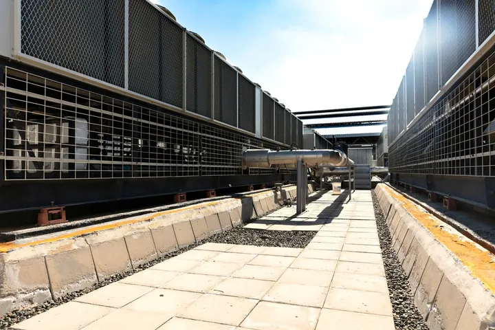 Large industrial cooling system with metal grilles and pipework outdoors in daylight